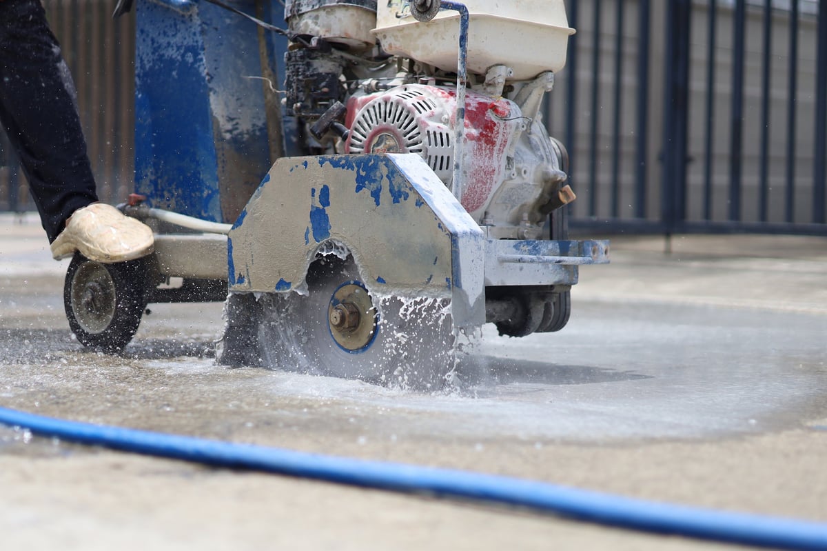 Walk-behind concrete cutter machine with spinning blade and water during concrete cutting