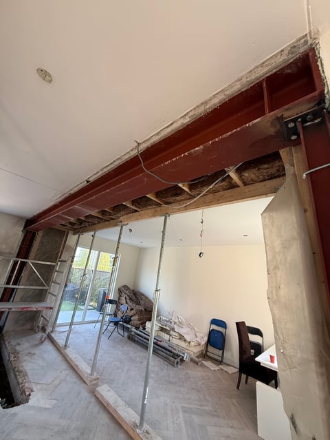 Interior renovation in progress with exposed red steel beam, temporary support structure, and chairs in empty room